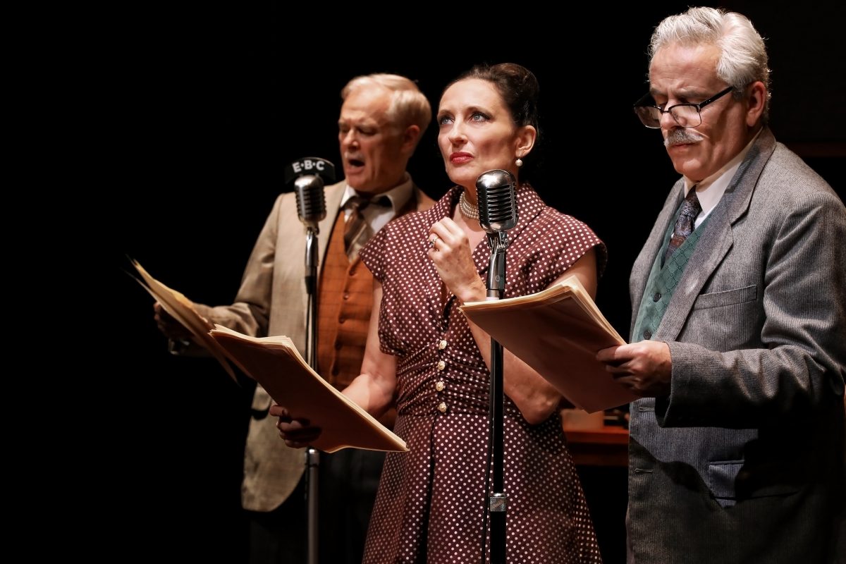 Three actors in vintage clothing stand at old-fashioned microphones, holding scripts. A man on the left sings or speaks passionately, while the woman in the centre and the man on the right read their lines.