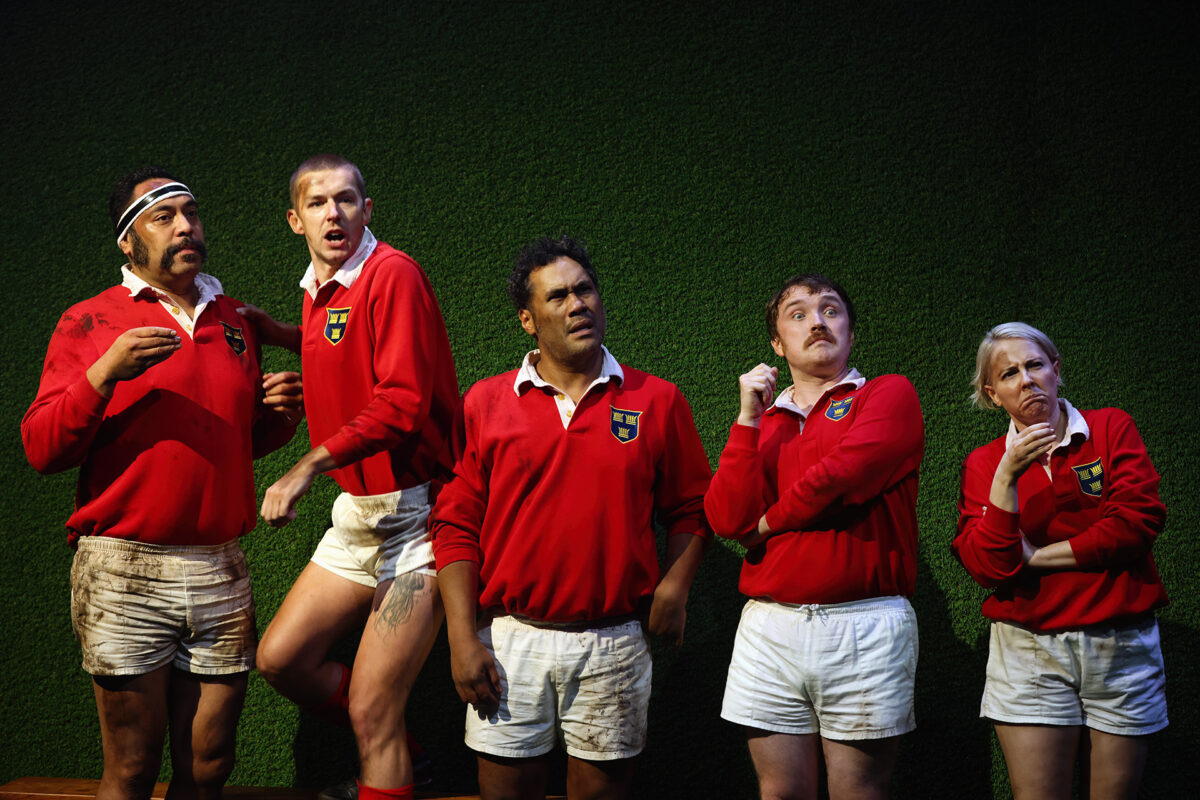 Five rugby players in red jerseys and white shorts stand in a row against a green background, each with a different puzzled or surprised expression, as if reacting to something off-camera.