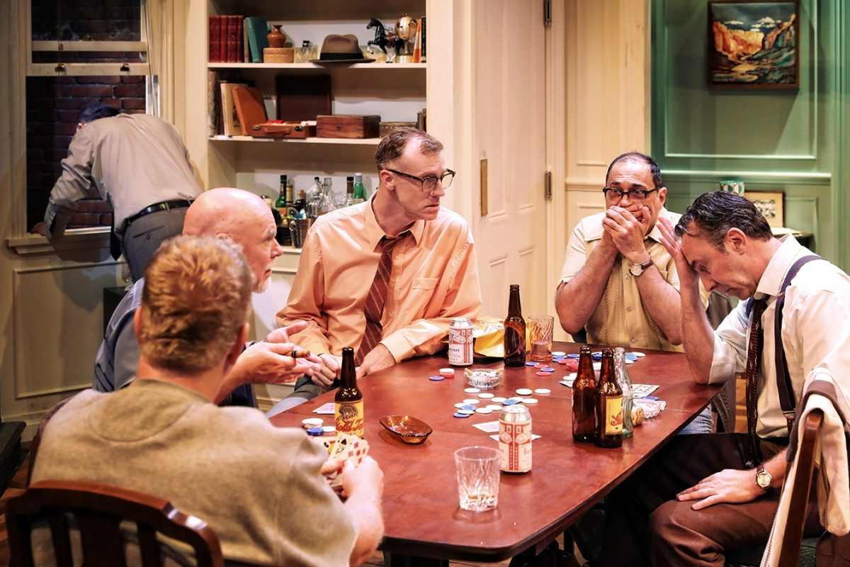 Six men sit around a table playing poker, with drinks and poker chips scattered. One man covers his mouth, another looks stressed, whilst another stands at a window in the background. The setting appears to be a cosy, lived-in room.
