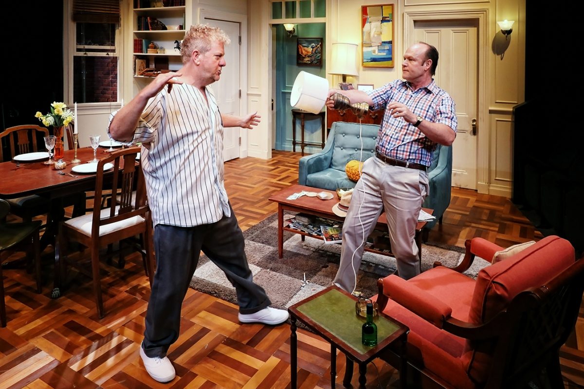 Two men in a lounge set appear to argue; one stands defensively with arms up, while the other gestures with a lamp. The room features a dining table, chairs, sofa, and a coffee table with decorative items.